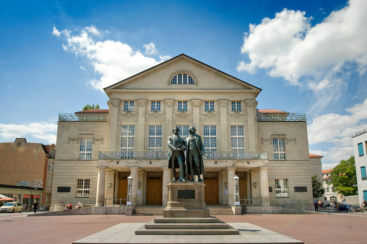 Zu sehen ist das Deutsche Nationaltheater Weimar. Im Vordergrund die Statue von Goethe und Schiller