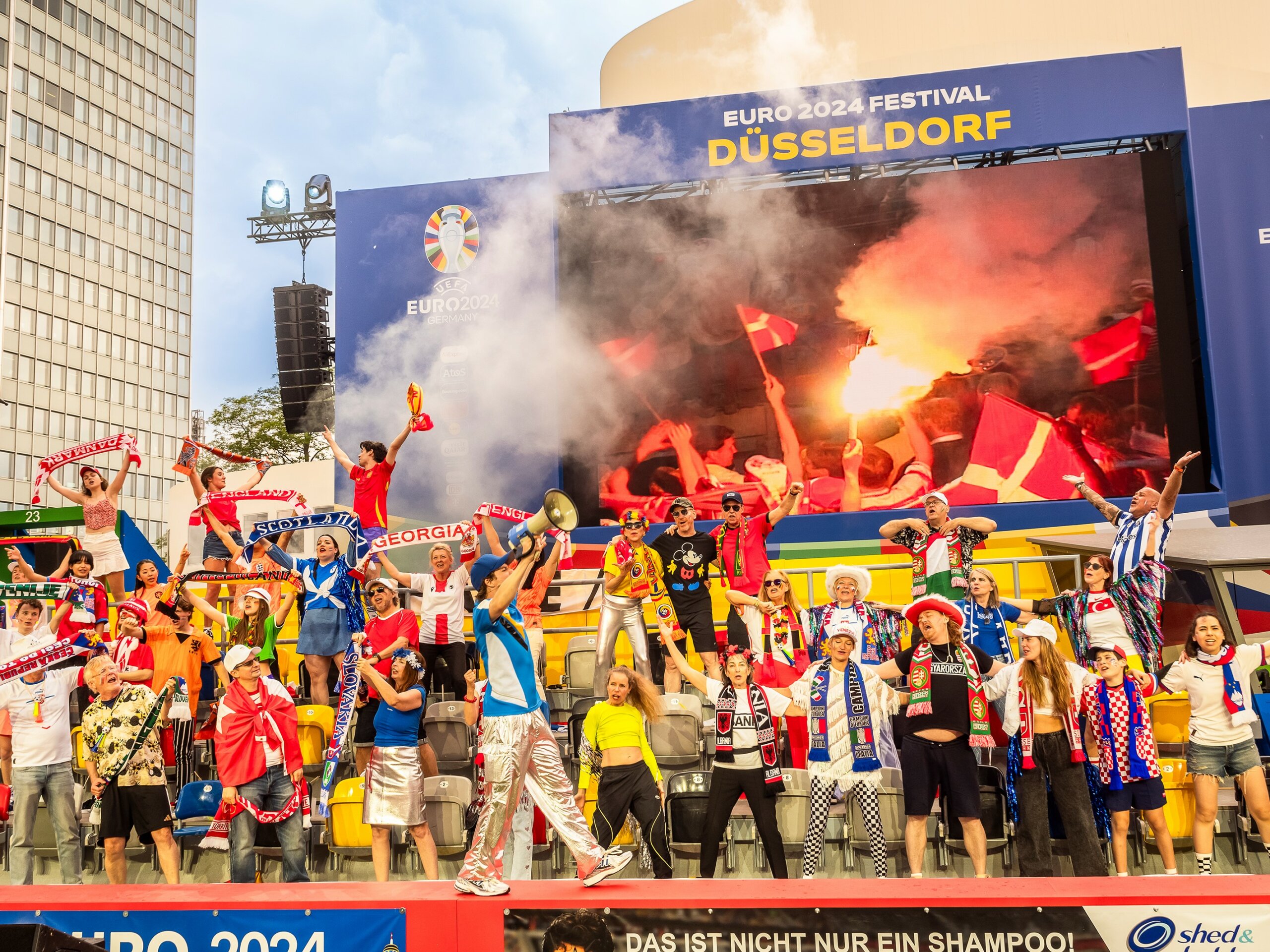 „Glaube, Liebe, Fußball“ vor dem Düsseldorfer Schauspielhaus. Zu sehen sind Fußballfans mit Schals auf einer Tribüne.