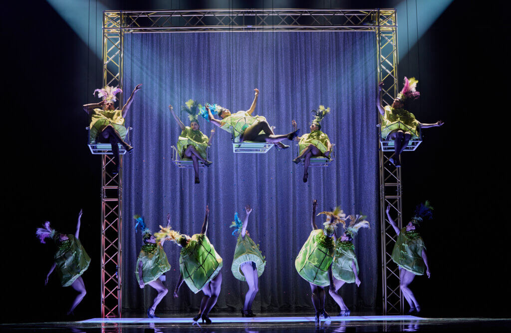 Ballett und Ensemble des Staatstheaters am Gärtnerplatz in grünen Kostümen, teilweise in der Luft schaukelnd